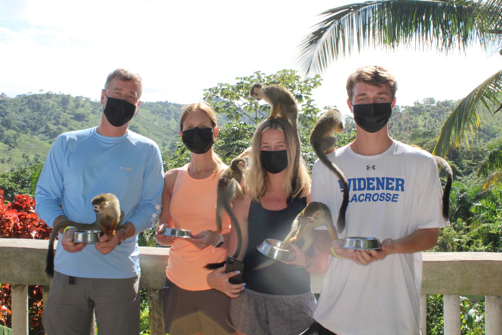 The family holding feeding bowls while squirrel monkeys climb on them