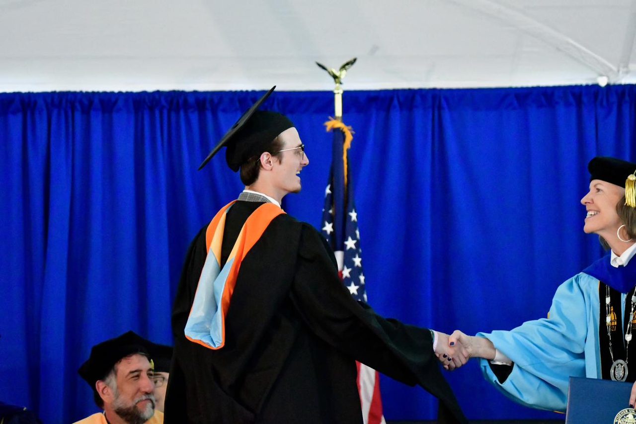 Cole crossing the stage in black robes at his master's graduation